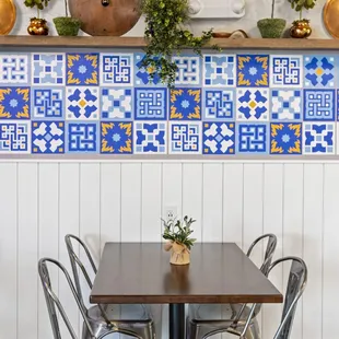 a table and chairs in front of a tiled wall
