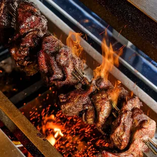meat being cooked on skewers on a grill