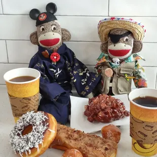 a couple of sock monkeys sitting next to a cup of coffee and doughnuts