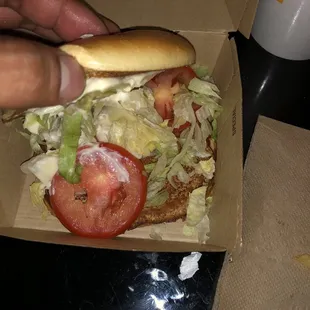 a hand holding a sandwich with lettuce and tomatoes