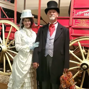 A sweet couple standing in front of the stage coach, all dressed up for a Night at the Museum.