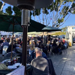 a crowd of people sitting at tables under umbrellas