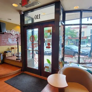 This is the front entrance of the coffee place with plenty of furniture. There is a stage for music. Outside is the downtown area.