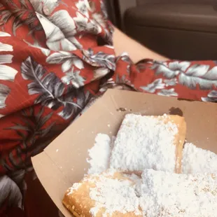 a woman holding a box of beignets