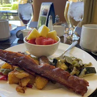 a plate of bacon, potatoes, and fruit