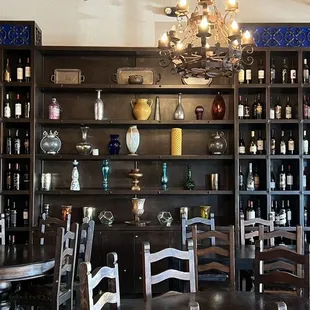 a table and chairs in front of a wall of wine bottles