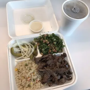 Beef schwerma plate with rice pilaf, tabouli, pickles and onions with an iced tea.