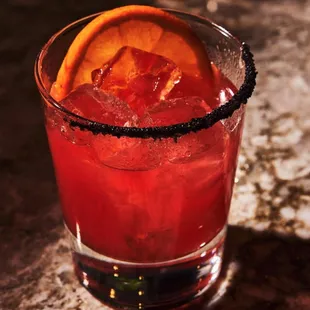 a red drink with a slice of orange on the rim