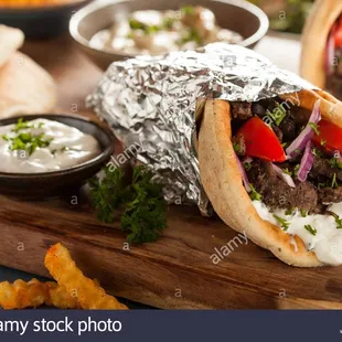 a beef pita wrapped in tin foil and served with fries and dips - stock image