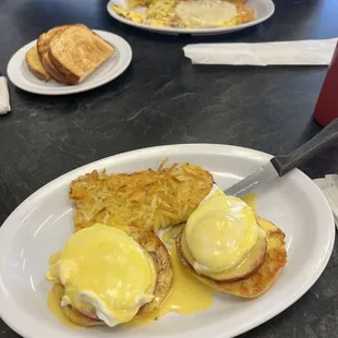 Eggs Benedict with hashbrowns in the front of the photo and meat and cheese omelet with white toast in the back.