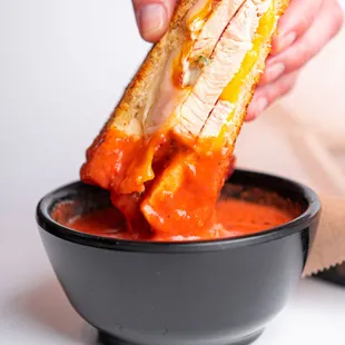 a person dipping a sandwich into a bowl of tomato sauce