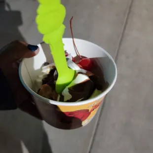 a person holding a cup of ice cream with a spoon sticking out of it