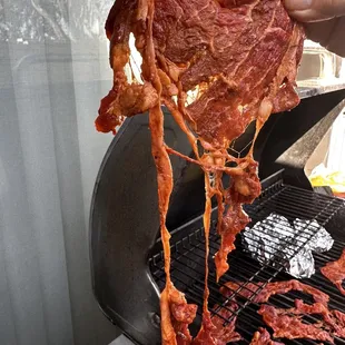 a person holding a piece of meat on a grill