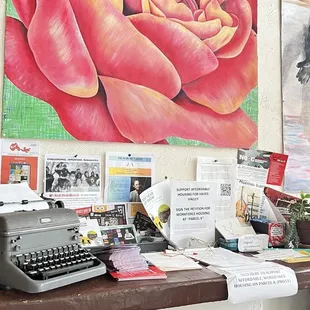 a desk with a typewriter and a painting of a rose