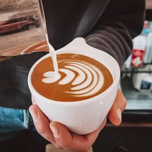 a person pouring milk into a cup of coffee
