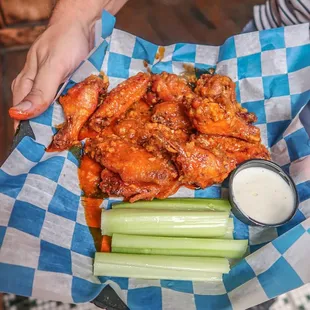 a person holding a basket of wings and celery