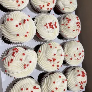 a dozen cupcakes with white frosting and red sprinkles