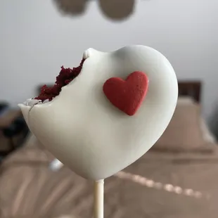 a hand holding a heart shaped cake on a stick