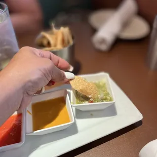 a person dipping a piece of bread into a bowl of dipping sauce