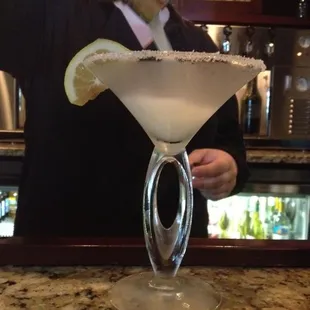 a bartender pouring a cocktail into a martini glass