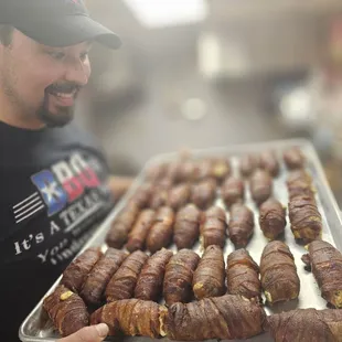 a man holding a tray of bacon wrapped in bacon