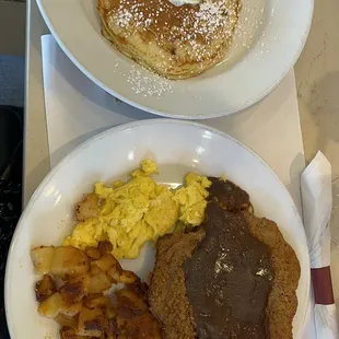 Pancake with syrup, Country fried steak with brown gravy, home fries and scrambled egg.