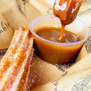 a hand dipping a donut into a bowl of caramel