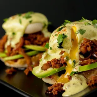 two eggs benedicts on a black plate