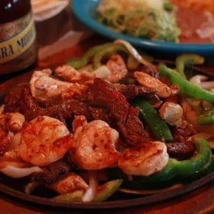 a plate of shrimp and peppers with a bottle of beer
