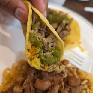 a person holding a tortilla over a plate of rice and beans