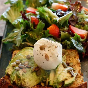 Avocado toast! On a crunchy pumpkin seed bread with pumpkin seed spread and a poached egg accompanied with rugula salad.