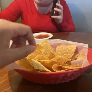 a woman sitting at a table with a bowl of chips and a cell phone