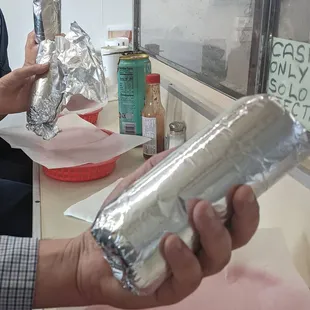 a man holding a sandwich wrapped in aluminum foil