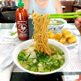 a man holding chopsticks above a bowl of noodles