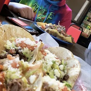 a boy sitting at a table with two tacos