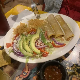 Seafood enchiladas with cheese sauce, rice with sliced avocados, lettuce and tomatoes.