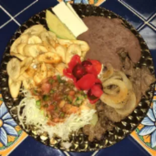 Carne asada con tajadas/Carne asada with fried green bananas, avocado, a slice of cheese, a cabbage salad with fried beans