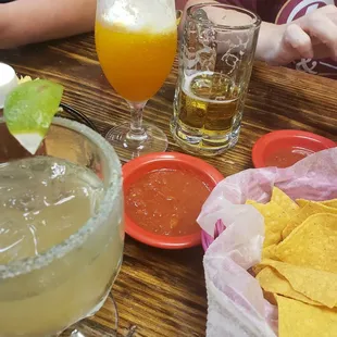 a glass of beer, a bowl of chips, and a glass of orange juice