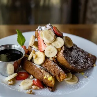a plate of french toast with strawberries, bananas, and powdered sugar