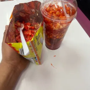 a hand holding a plastic cup with a straw and a bag of salsa