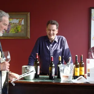 two men standing at a bar with bottles of wine