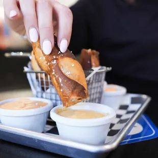 a person dipping a pretzel into dipping sauces