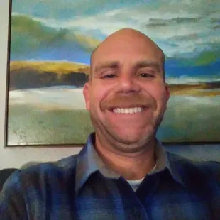 a man smiling in front of a painting