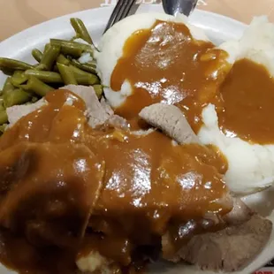 a plate of food with gravy, mashed potatoes and green beans