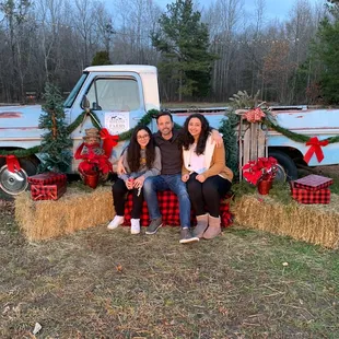 a family sitting on hay bales in front of a truck decorated for christmas