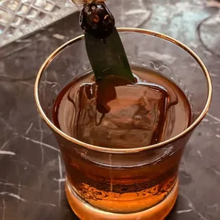 a glass of whiskey with a green leaf sticking out of it