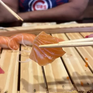 a person holding chopsticks over a piece of sushi