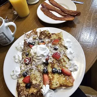 a plate of french toast with berries and whipped cream