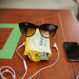 a pair of sunglasses, ear buds, and a cell phone on a table