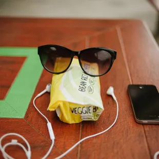 a pair of sunglasses, ear buds, and a cell phone on a table